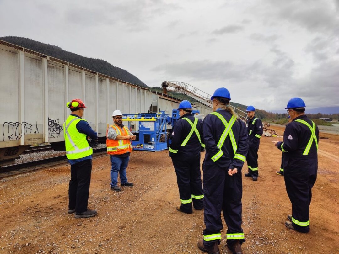 People in safety gear in front of a railcar loading wood pellets.